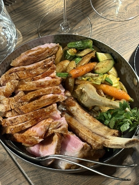 Uppskuren kotlettrad på ben i en järnpanna, med grillade sommarprimörer som zucchini, morötter och sparris
