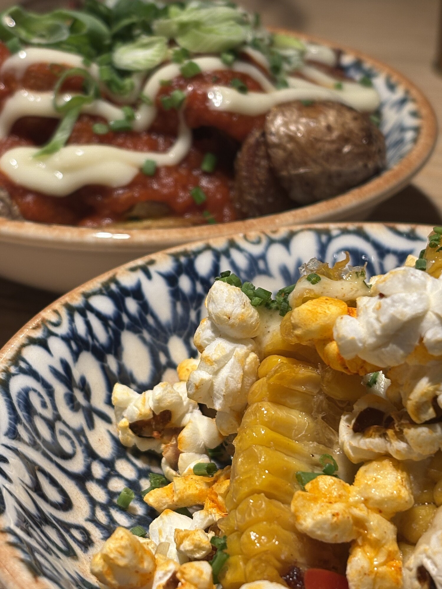 Grillad majskolv i mönstrad skål, täckt med rökt paprikasmör, popcorn och gräslök