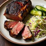 Grillad pata negra-karré med mörk stekyta, delvis uppskuren i rosa skivor, serverad med kålsallad och gurkskivor