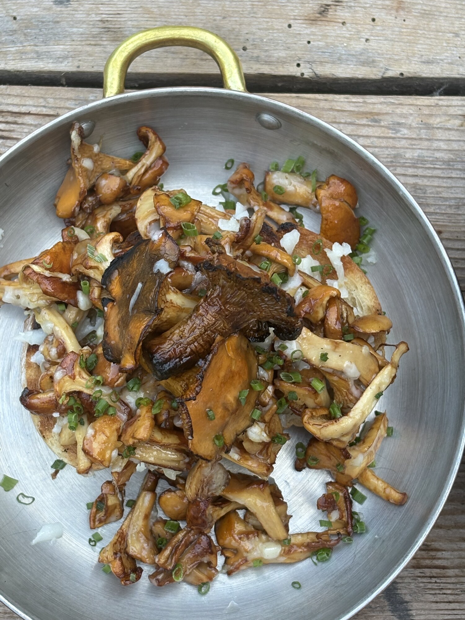 Grillade kantareller med hackad vitlök och gräslök i en stålpanna på ett grått trädäck
