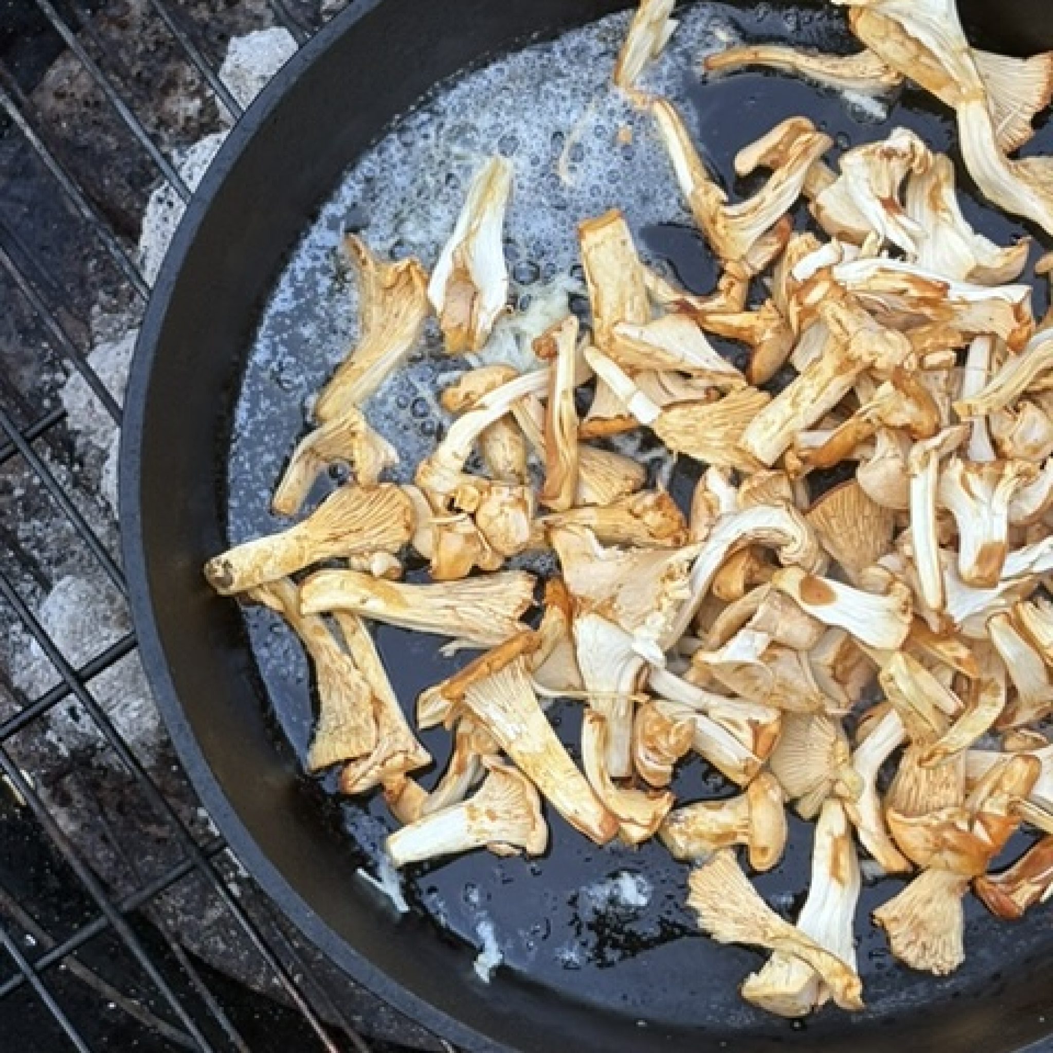 Kantareller som steks i smör i en svart panna över grillen