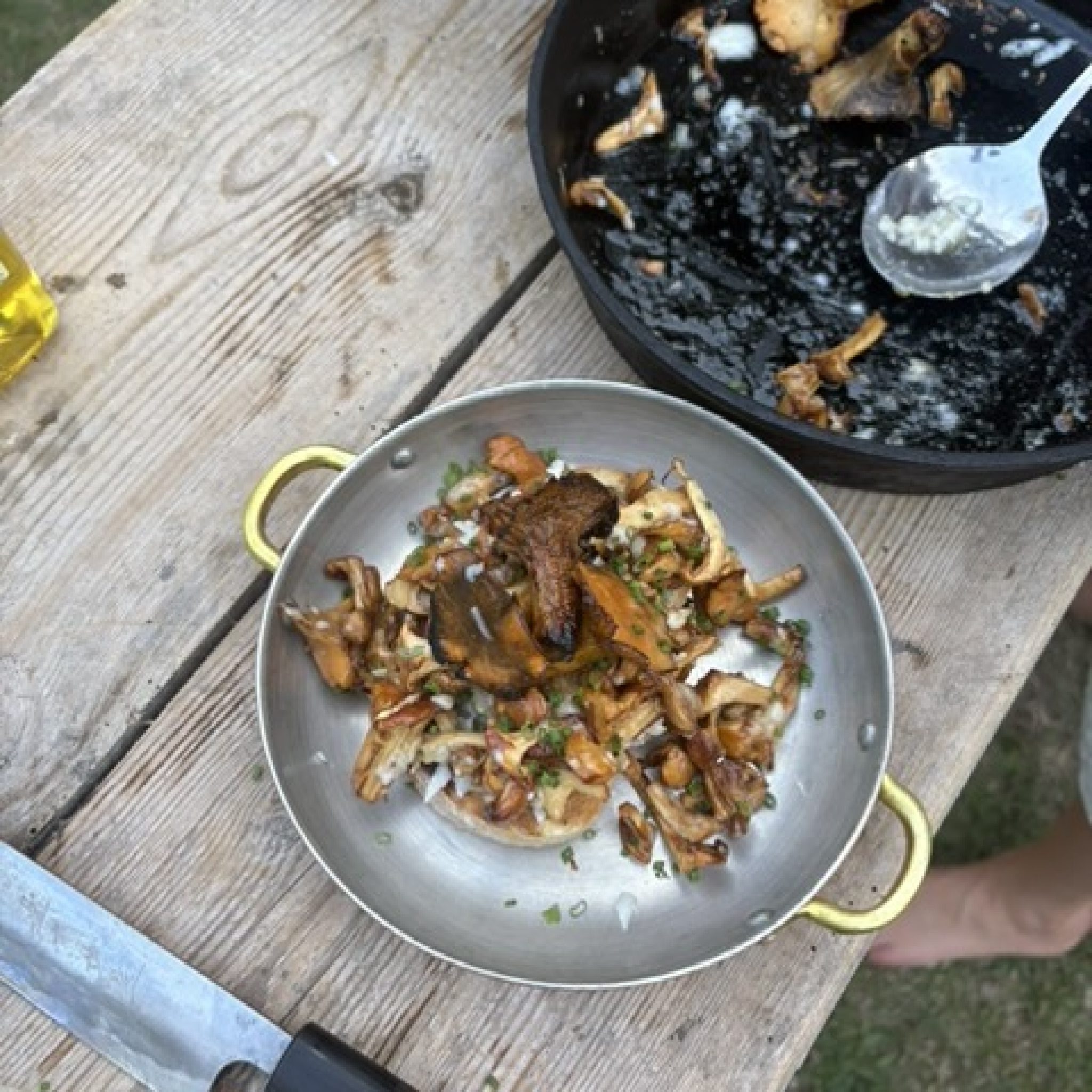 Grillade kantareller med gräslök i en liten stålpanna på ett träbord, med stekpannan bredvid