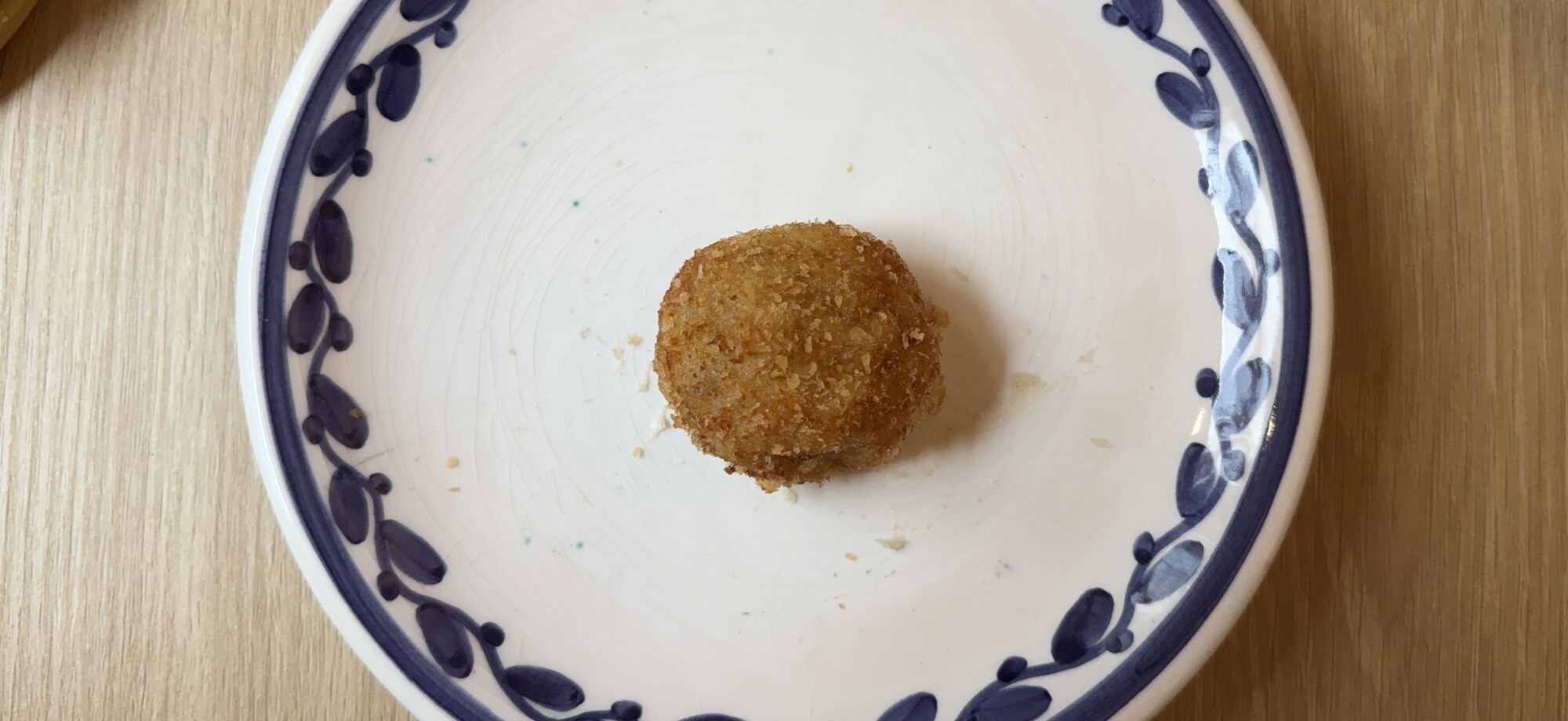 En enda gyllenbrun krokett på vit tallrik med blå bladbård