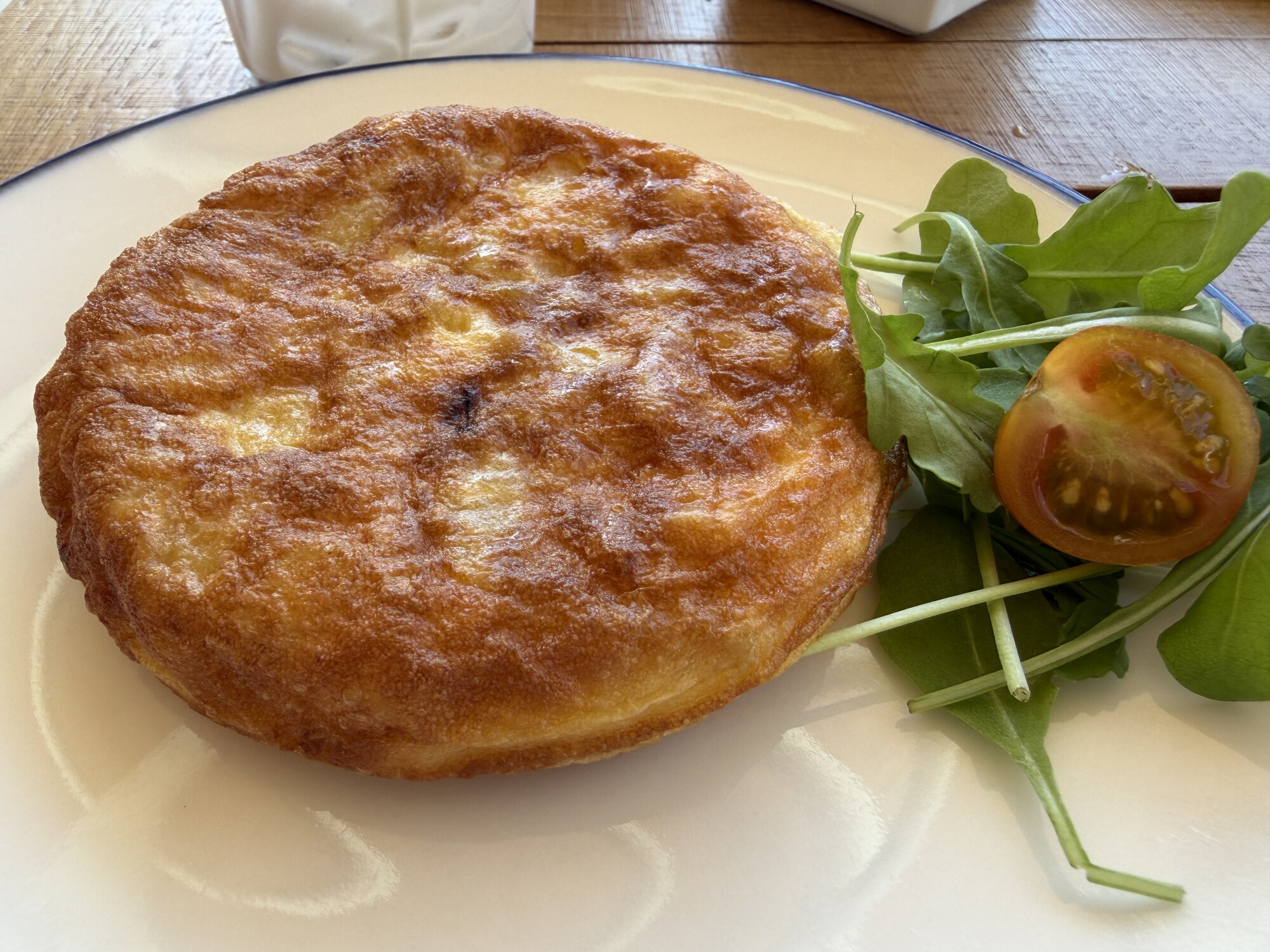 Rund mini-tortilla med gyllene stekyta på vit tallrik, serverad med ruccola och en halverad körsbärstomat