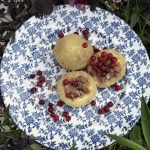 Två kroppkakor på blommig blåvit tallrik, en delad så köttfyllningen syns, strödda med röda lingon