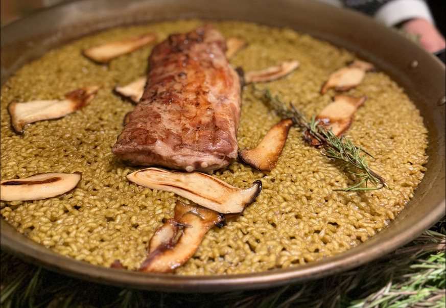 Paella arroz seco i stor panna med torrt gyllenbrunt ris, en bit grillat ibericokött, skivad svamp och rosmarin