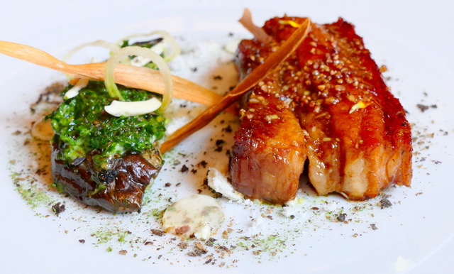 Grillad presa ibérica med glaserad yta på vit tallrik, med grön gremolata på en grillad grönsak bredvid