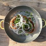 Grillat surdegsbröd med varm sobrasada i en liten stålpanna, toppat med papperstunn lök och gräslök