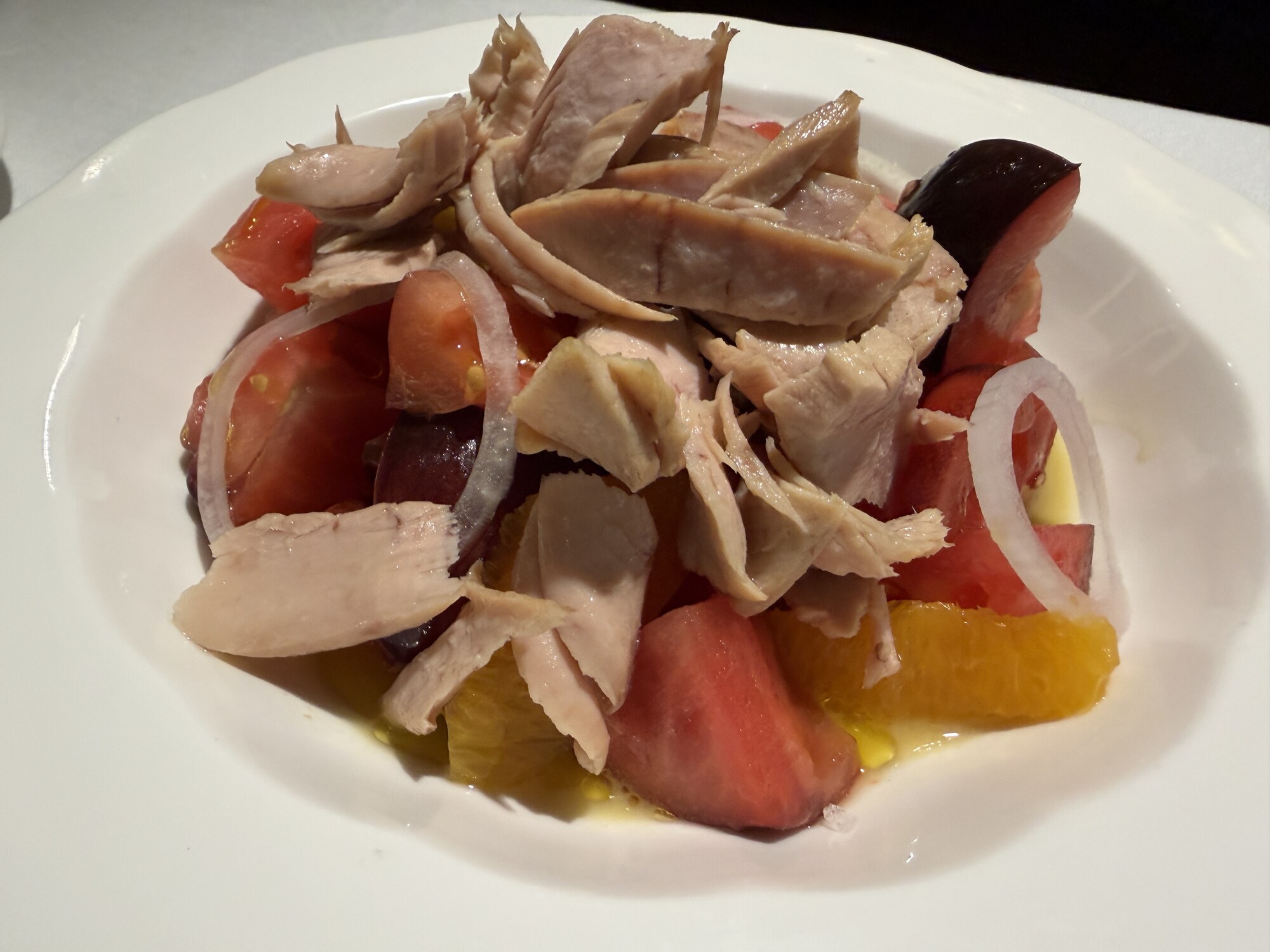 Tomatsallad i djup vit tallrik med tonfiskbitar av ventresca, tomatklyftor, apelsin och tunt skivad rödlök i olivolja