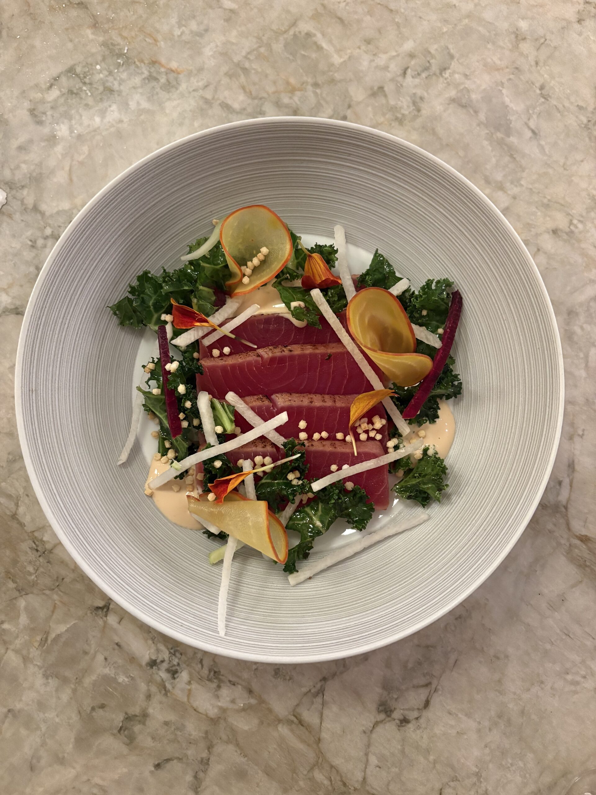 Skivad grillad tonfisk med röd kärna i djup vit skål, med grönkål, tunna stavar av gulbeta, rödbeta och poppat ris