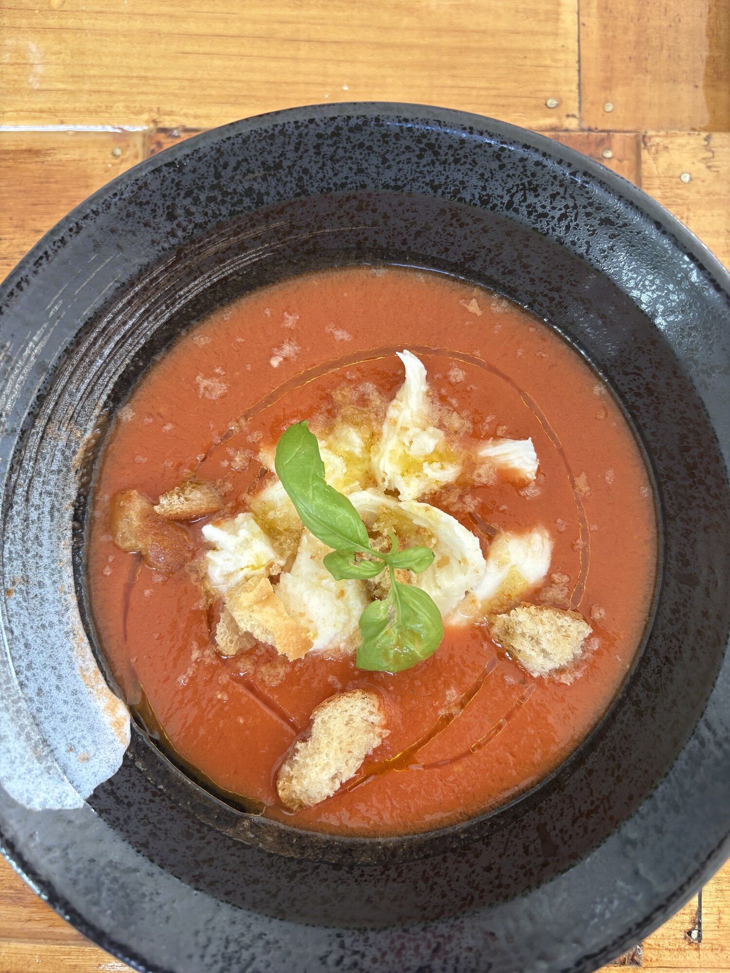 Gazpacho med getostkräm, krutonger och basilika i svart skål
