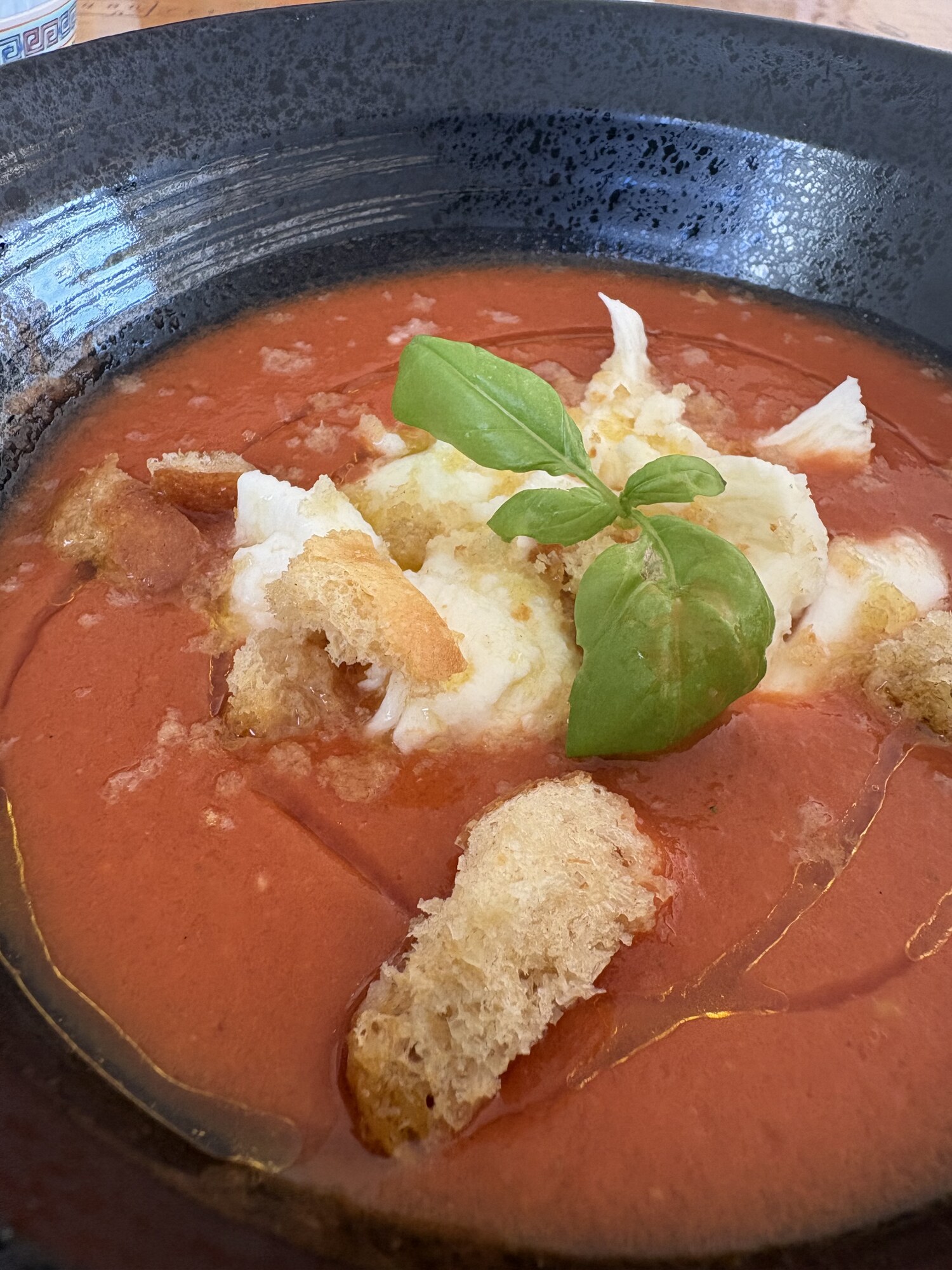 Närbild på gazpacho med getostkräm, krutonger och basilikaskott
