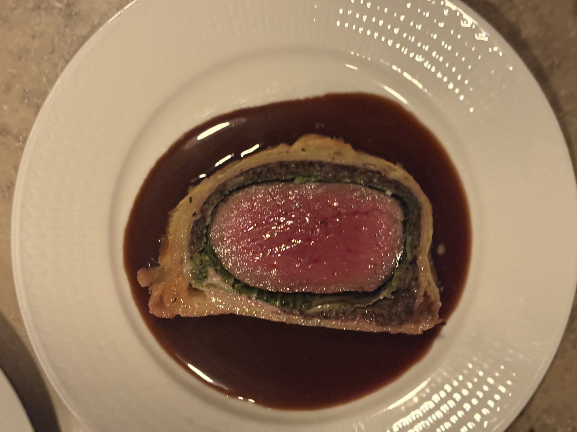Skiva biff Wellington i genomskärning med rosa kött, örtlager och smördeg, i en spegel av mörk rödvinssås