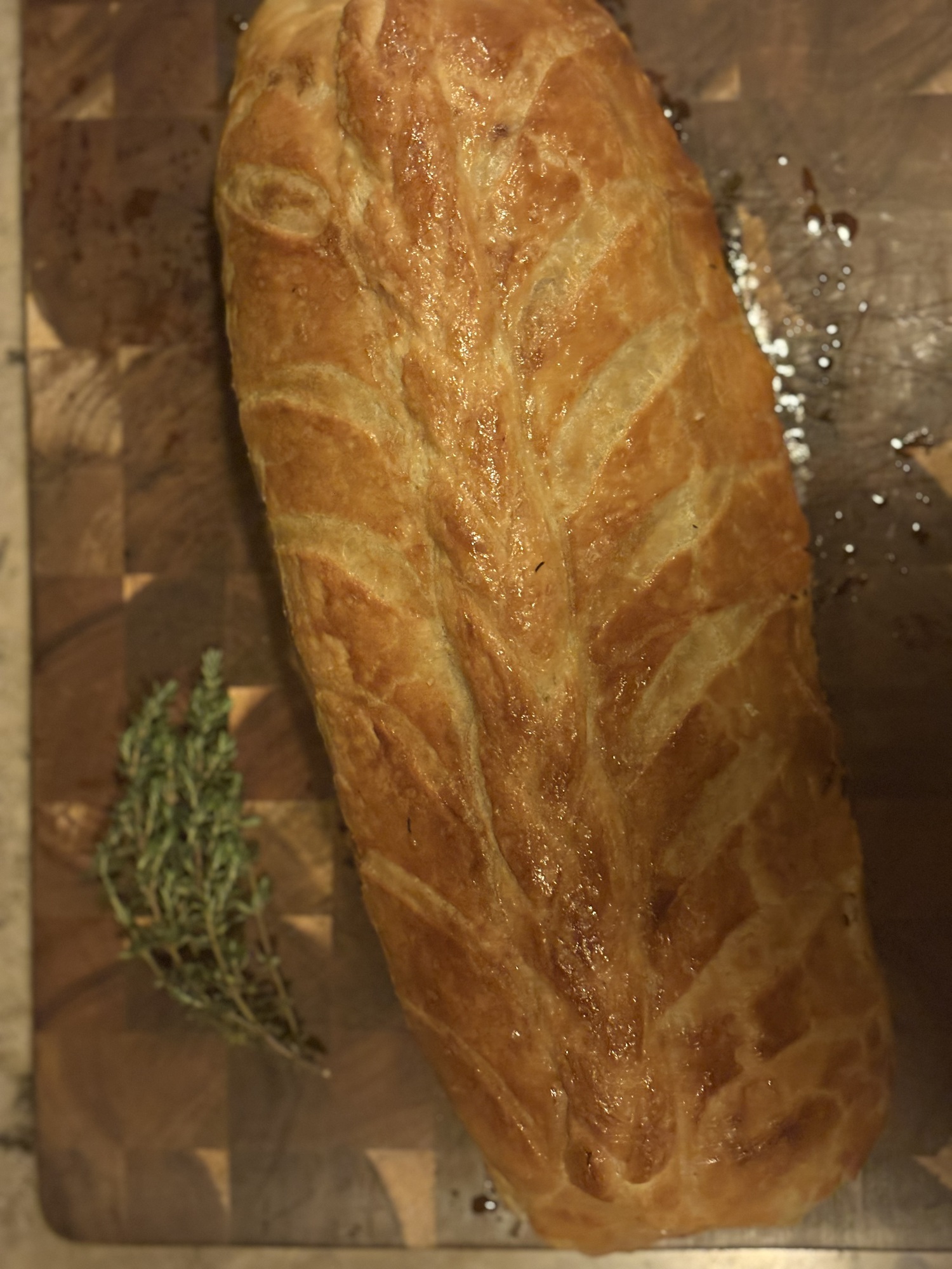 Hel biff Wellington med gyllenbrun mönstrad smördeg på en skärbräda, med en kvist timjan bredvid