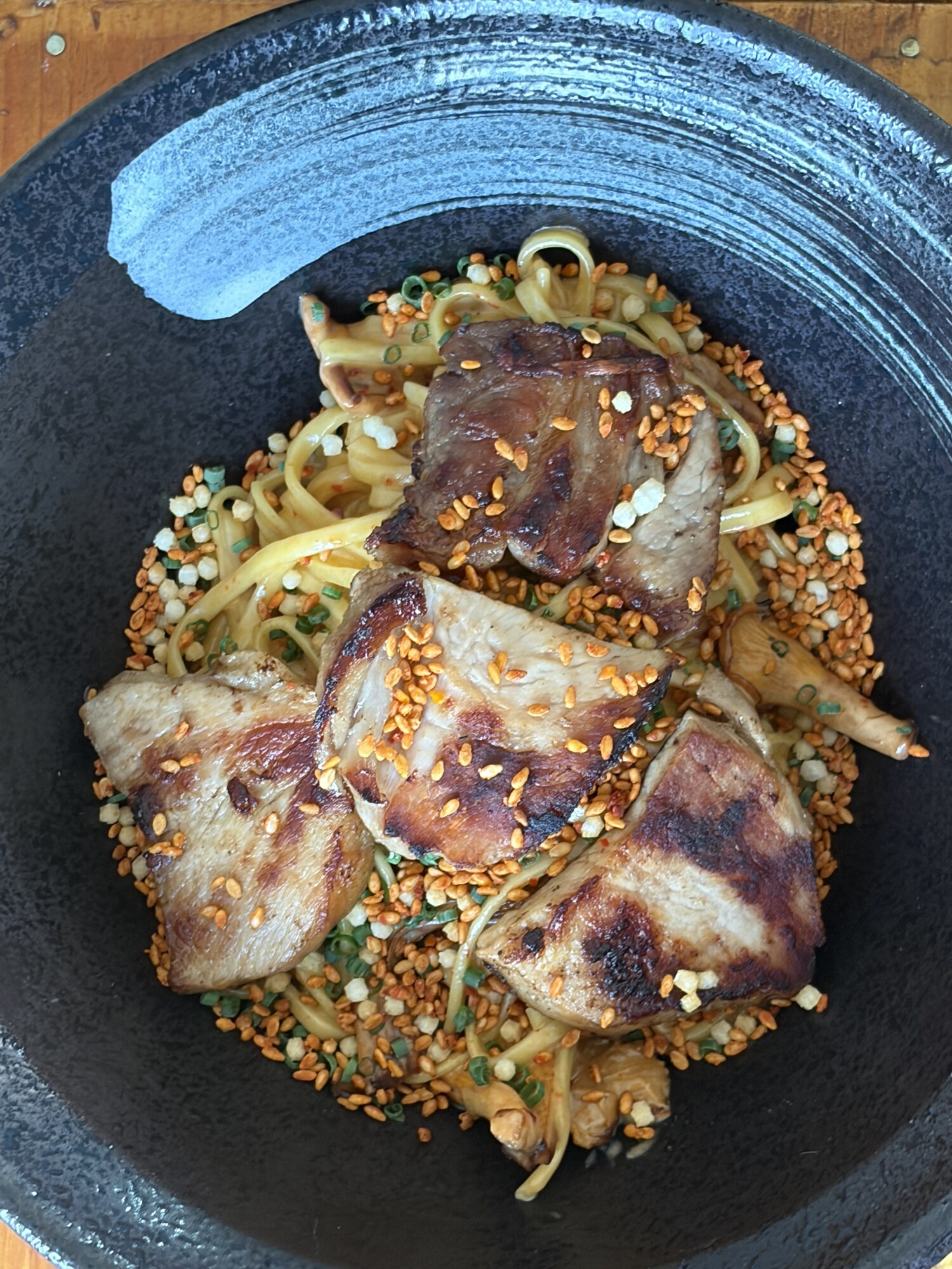 Äggnudlar i svart skål toppade med skivad pata negra, rostad sesam och poppat ris
