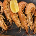 Grillade gambas med skal på svart fat med citronklyfta
