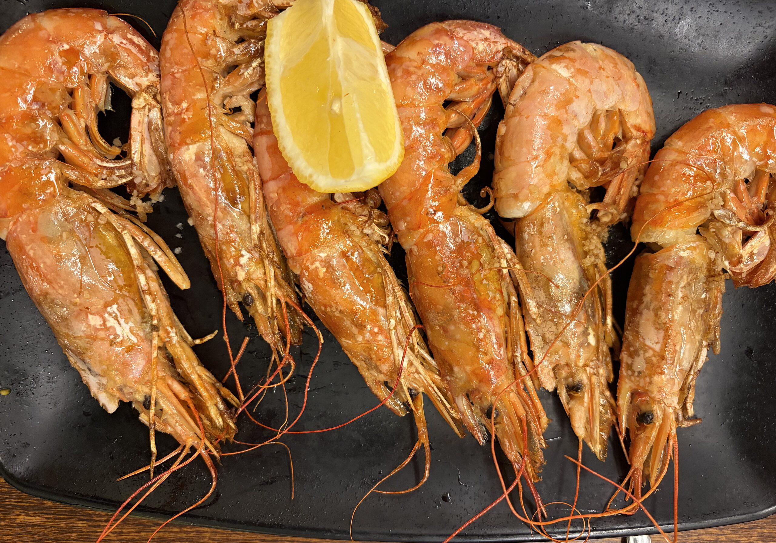 Grillade gambas med skal på svart fat med citronklyfta