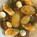 Rökta boquerones med kokt färskpotatis, halverade ägg, klickar av Torta del Casar och dill i olivolja på vit tallrik
