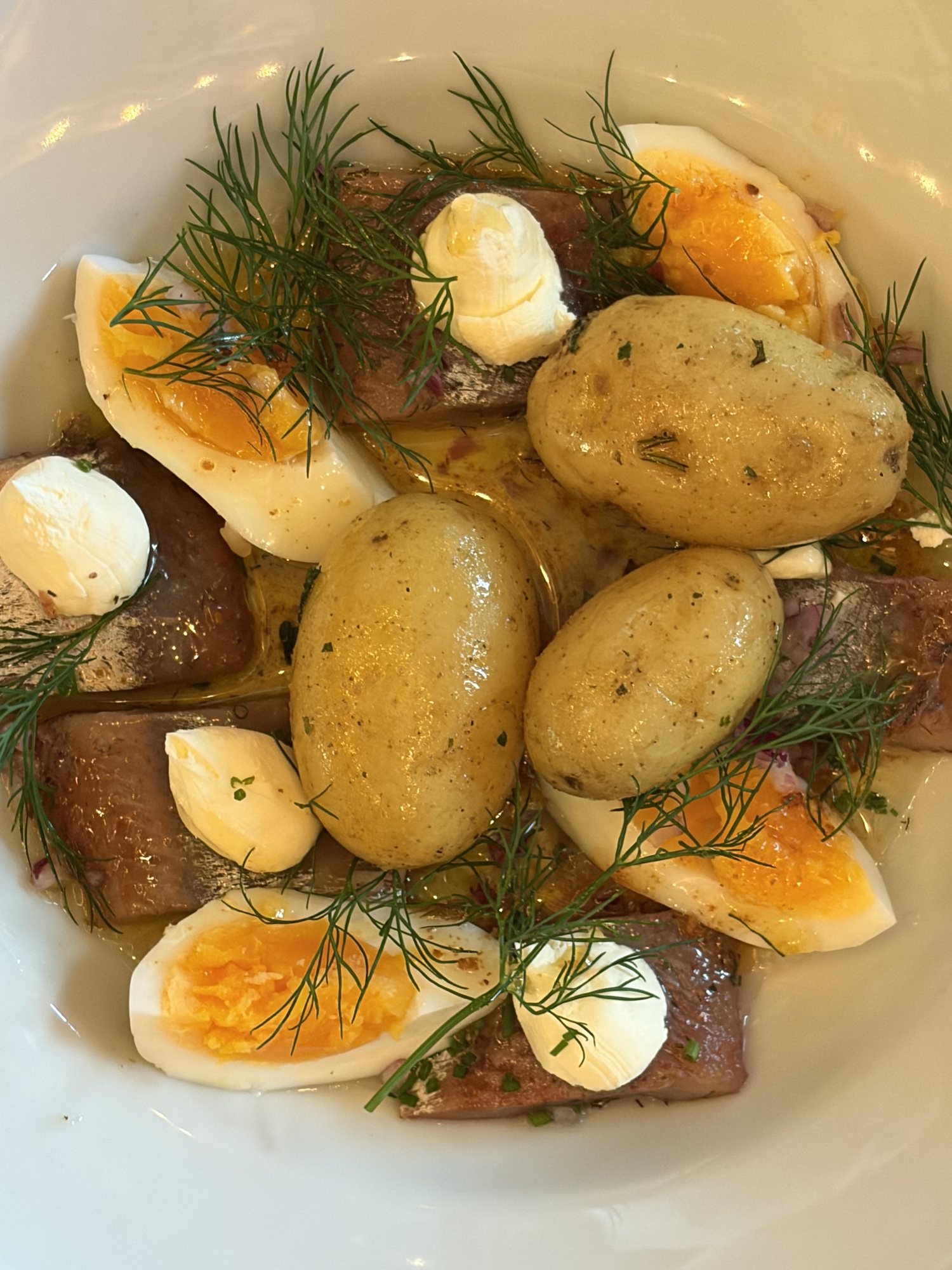Rökta boquerones med kokt färskpotatis, halverade ägg, klickar av Torta del Casar och dill i olivolja på vit tallrik