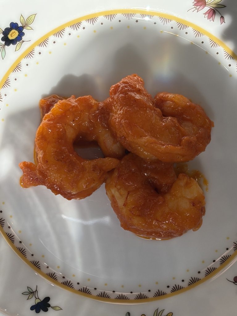 Tre stora skalade räkor i blank orangeröd salsa brava på en blomstermönstrad tallrik