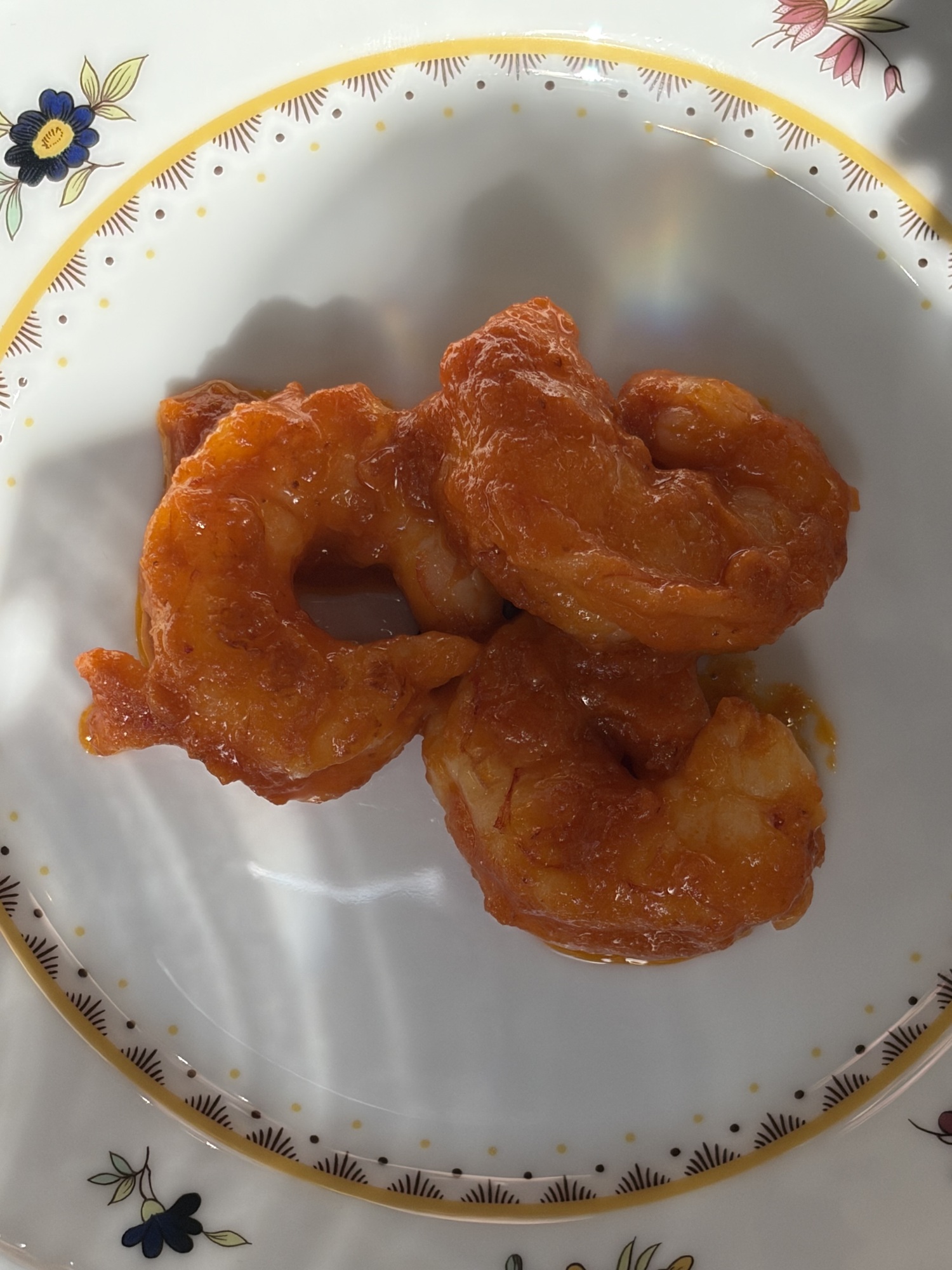 Tre stora skalade räkor i blank orangeröd salsa brava på en blomstermönstrad tallrik