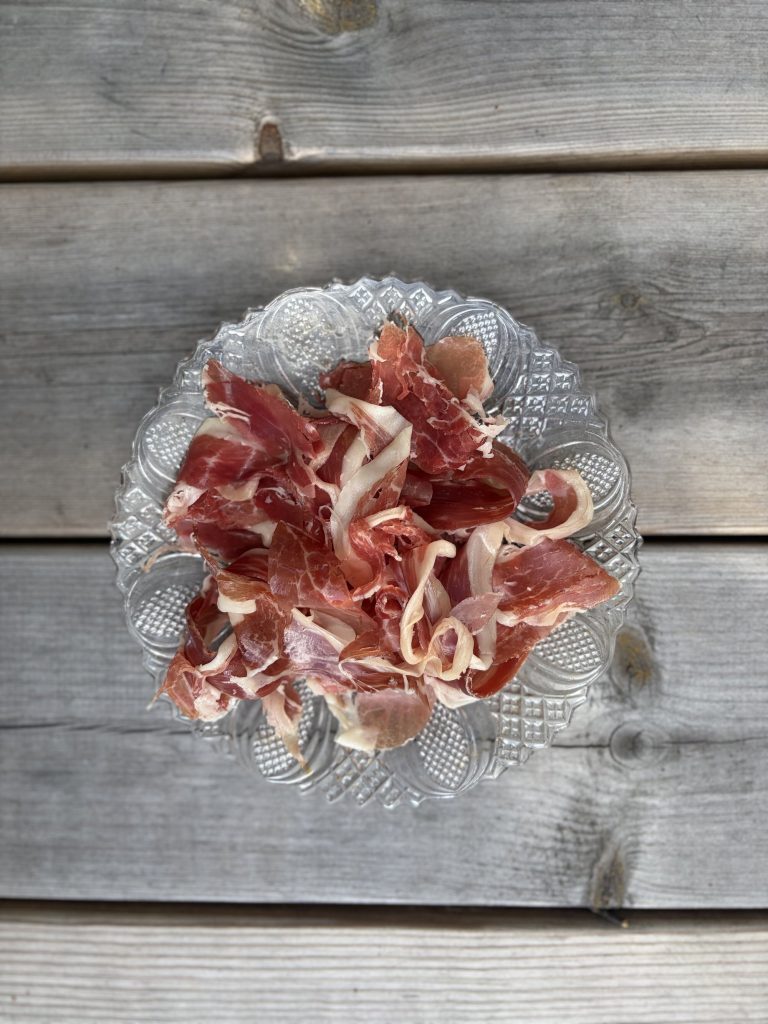 Handskuren jamón ibérico de bellota rufflad på glasfat