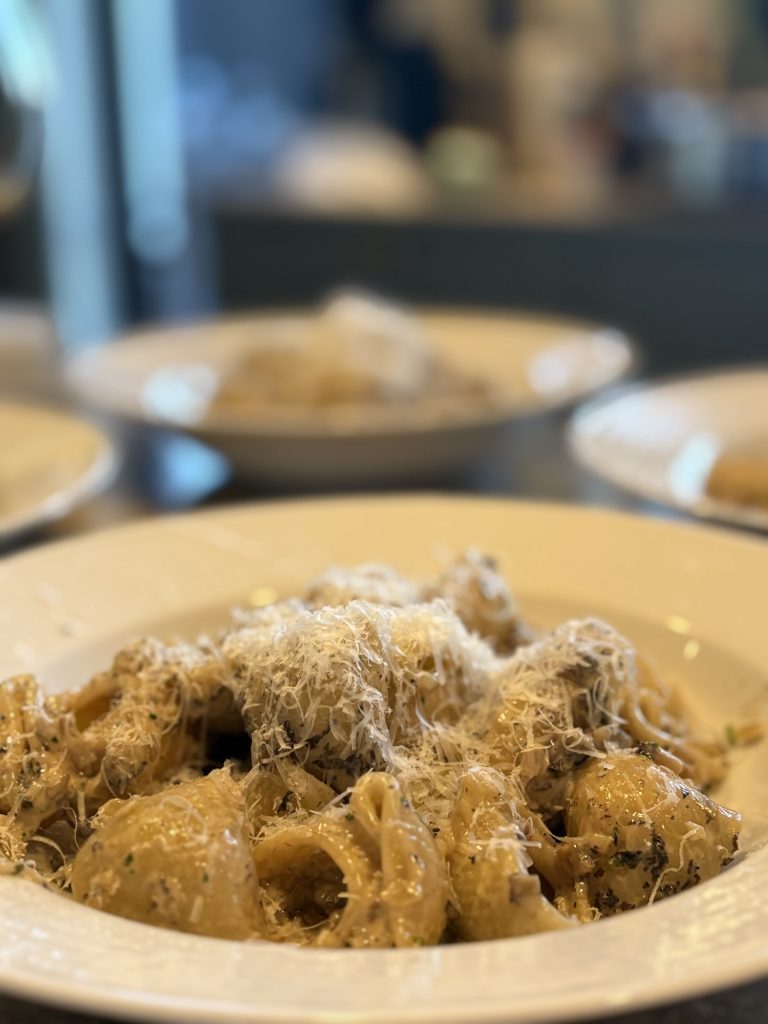 Krämig pasta med rikligt riven manchego och mörka örtprickar i djup vit tallrik