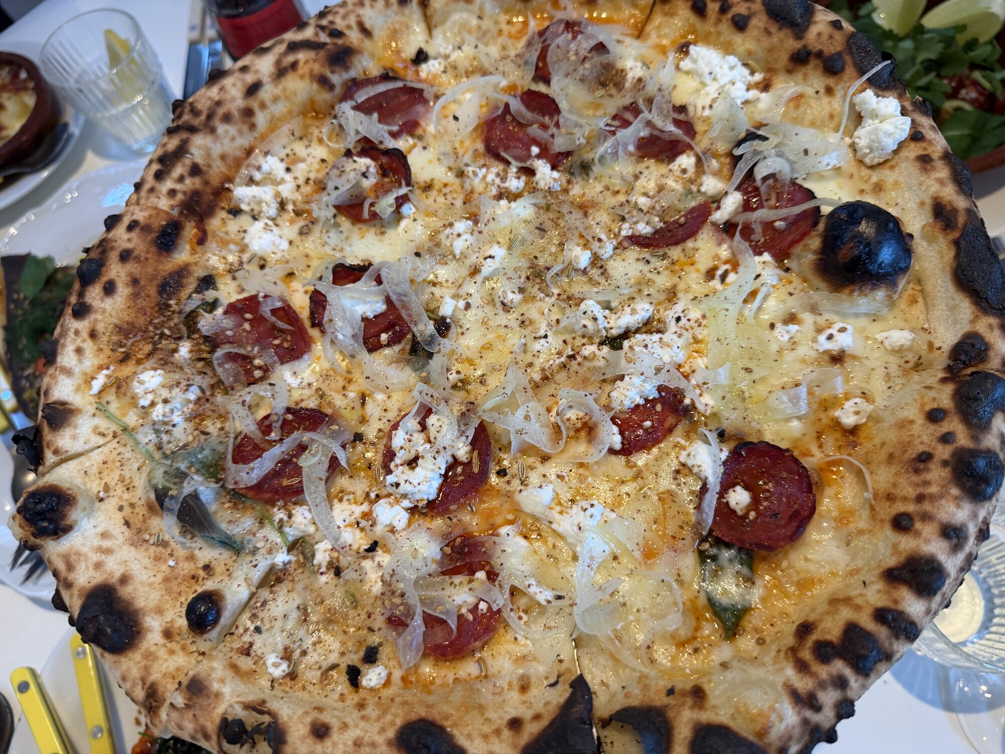 Vit pizza med skivad chorizo, klickar av getost, hyvlad lök och fänkålsfrö