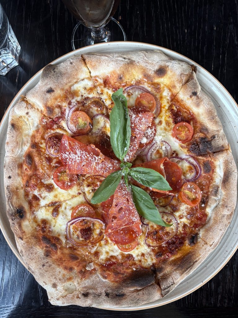 Nybakad pizza med tomatsås, ost, körsbärstomater, rödlök, skivor av pata negra och färsk basilika i mitten