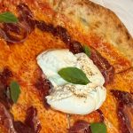Nybakad pizza med tomatsås, skivor av jamón ibérico, en klick vit ostkräm och basilikablad