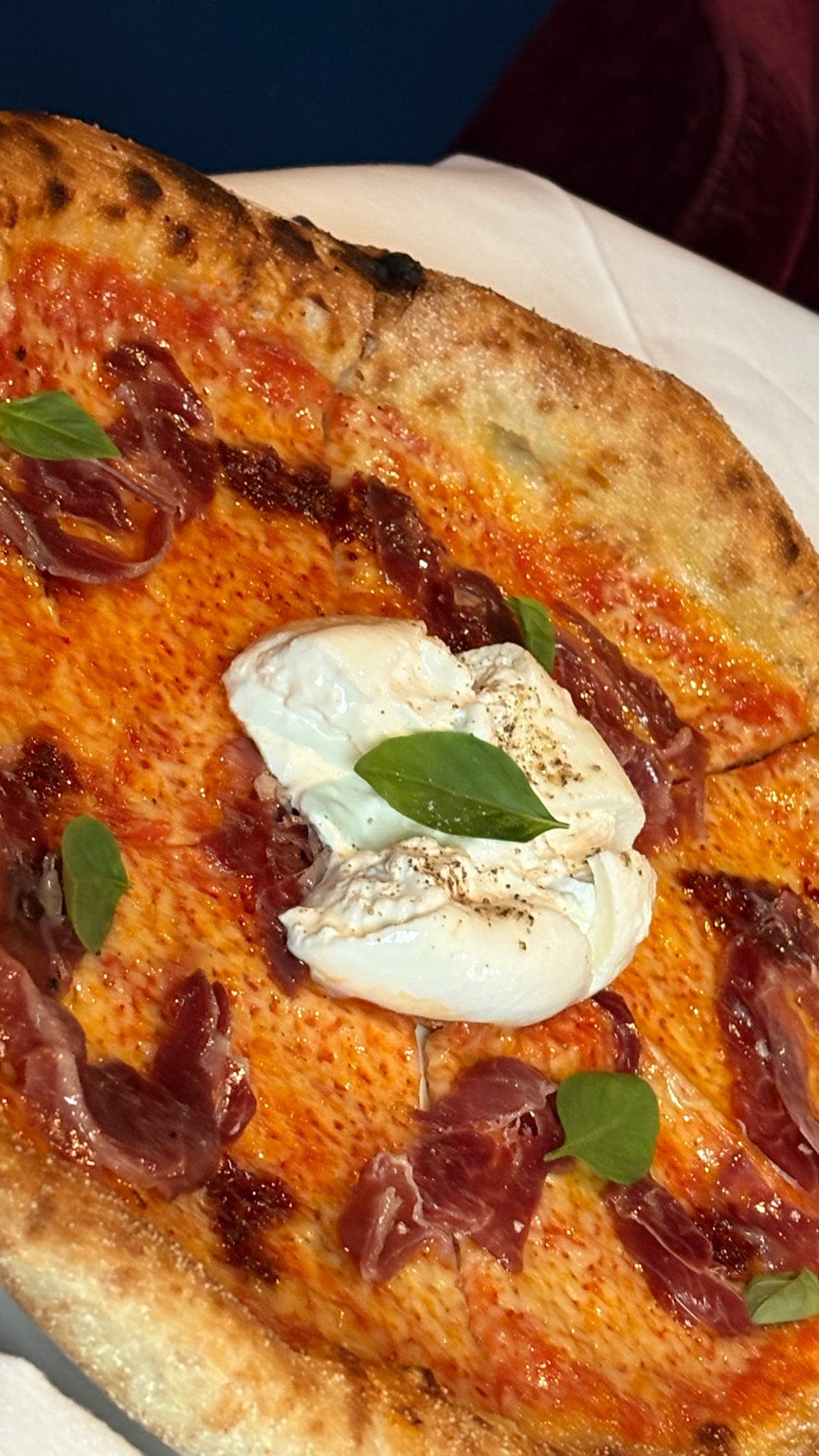 Nybakad pizza med tomatsås, skivor av jamón ibérico, en klick vit ostkräm och basilikablad
