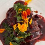 Hjortrygg med lingonsås, örter och ätbara blommor på vit tallrik