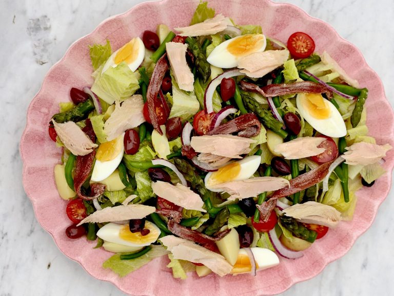 Salade niçoise med tonfisk, ansjovis, ägg och oliver på ett rosa fat