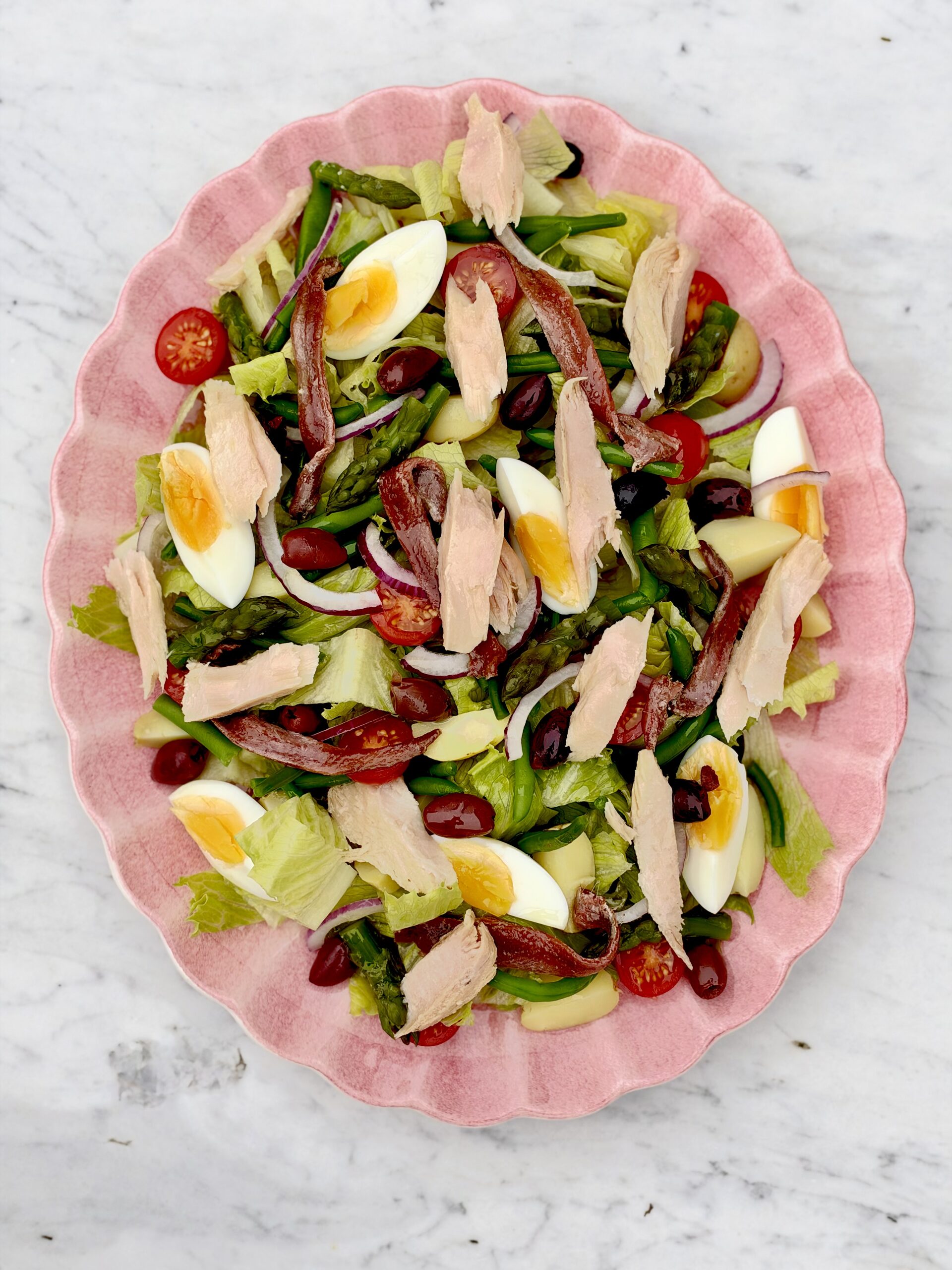 Salade niçoise med tonfisk, ansjovis, ägg och oliver på ett rosa fat