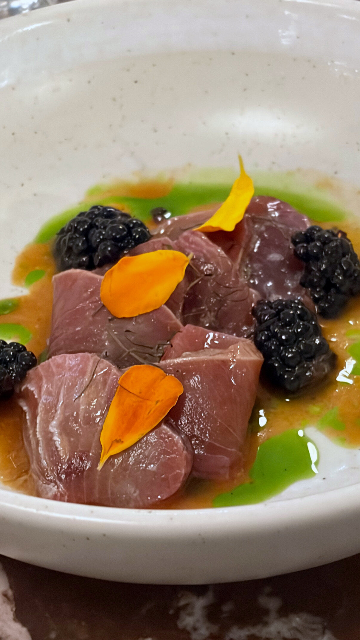 Tonfiskcrudo med björnbär, örtolja och tagetesblad i en djup tallrik