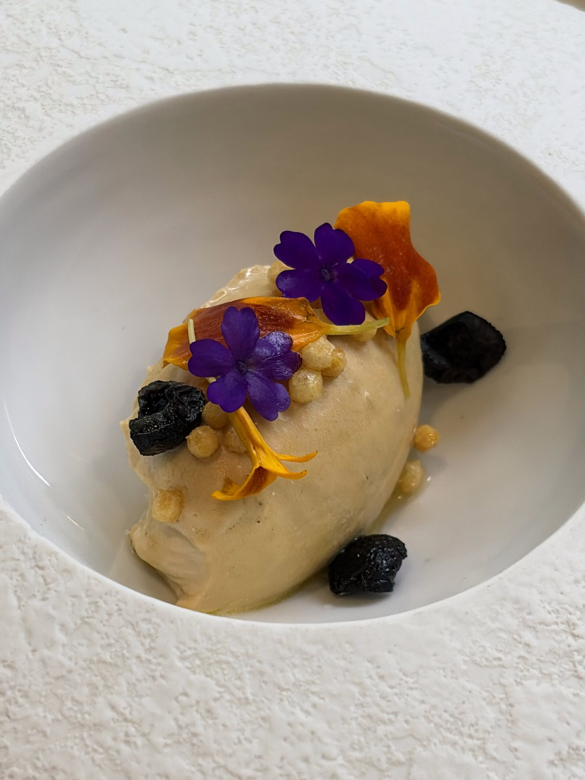Quenelle av vispad anklever med torkade svarta oliver, poppat ris och ätbara blommor